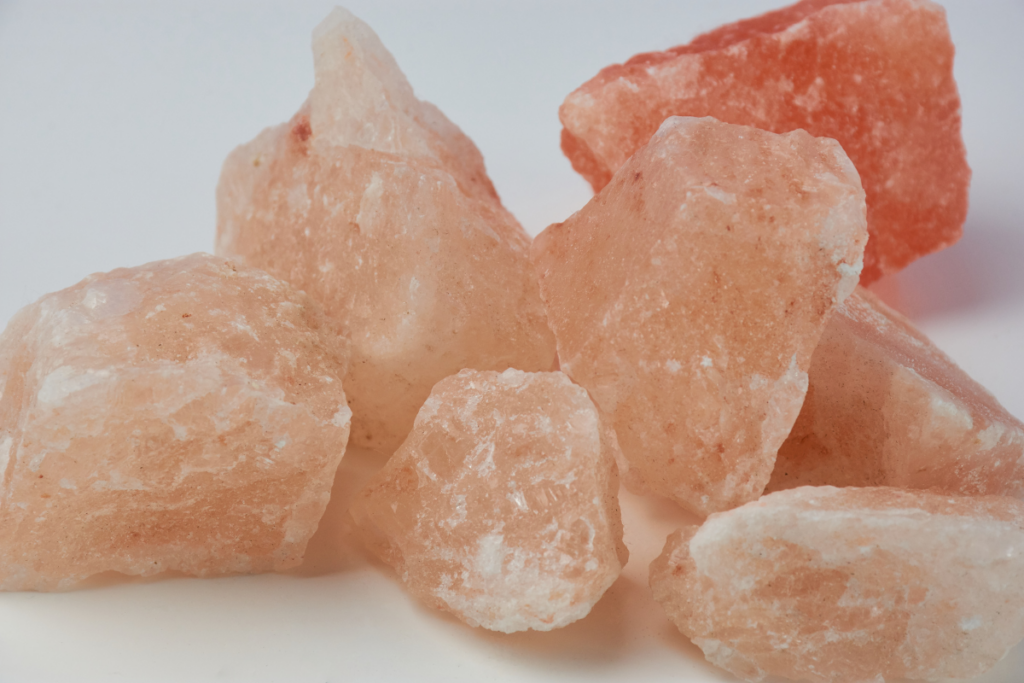Several chunks of unrefined pink Himalayan salt crystals on a white background.